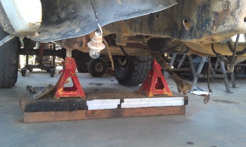 1978 Ford Bronco - The underside of a vehicle is elevated on red jack stands, revealing its suspension and drivetrain parts.