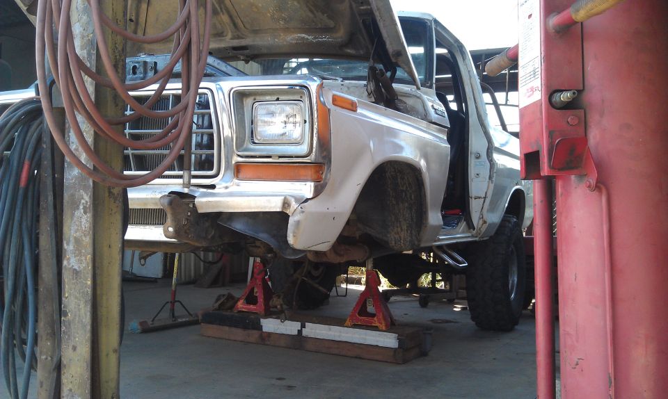 White Ford truck on jack stands, front end visible, hood open, grille and headlight assembly intact