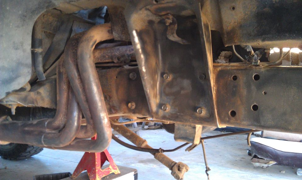 1978 Ford Bronco frame with rusty exhaust manifold, jack stands, and part of a seat visible