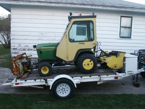 1966 Ford Bronco - A green and yellow tractor with a cab is loaded onto a trailer, equipped with a snow blower attachment.