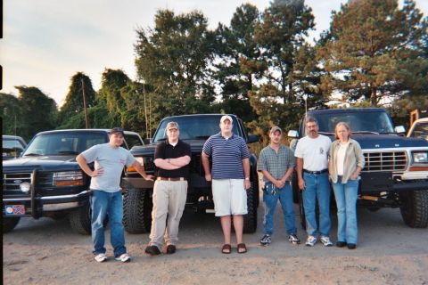 1988 Ford Bronco - Five people pose with three trucks in an outdoor setting.