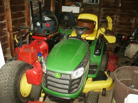 1966 Ford Bronco - John Deere lawn tractor parked with gas cans, shop vac, and other equipment in a shed.