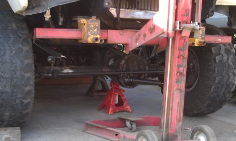 1978 Ford Bronco - The underside of a vehicle is shown, supported by jack stands and mechanical equipment.
