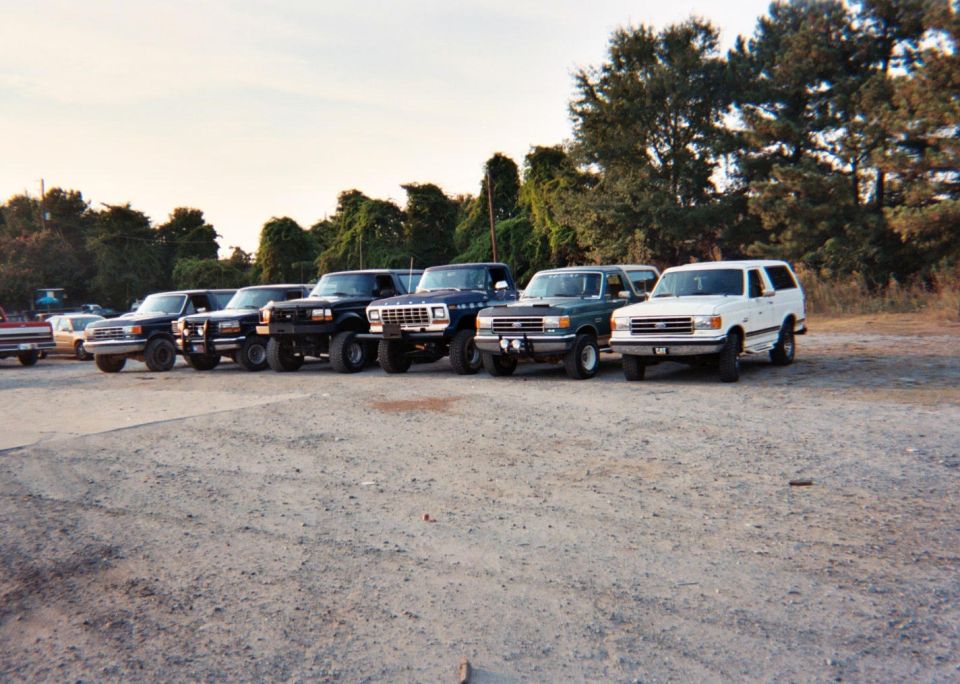 White SUV parked in a line of trucks, side view. License plate visible