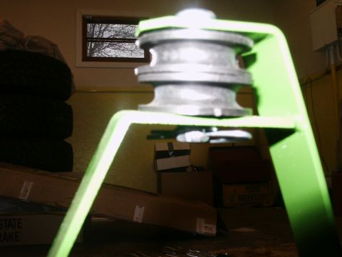 1966 Ford Bronco - A green metal bracket with a pulley wheel is shown, with storage items in the background.