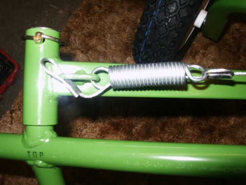 1966 Ford Bronco - Close-up of a green metal frame with a spring and a tire in the background.