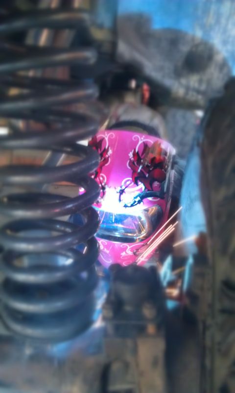 1978 Ford Bronco - A person is welding a vehicle component, sparks flying, with a large spring in the foreground.