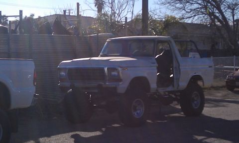 1978 Ford Bronco - A white 1978 Ford Bronco is parked outdoors with its doors off and suspension lifted.