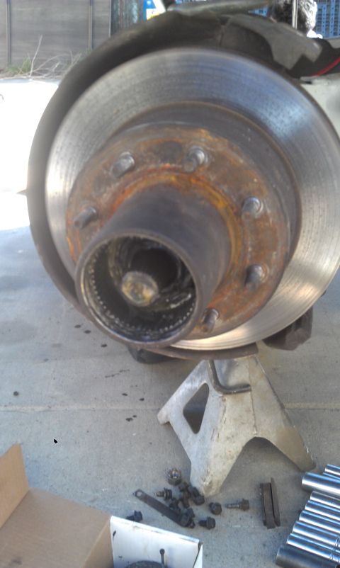 1978 Ford Bronco - Vehicle brake rotor and hub assembly on a jack stand with hardware on the ground.