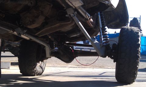 1978 Ford Bronco - The underside of a heavily modified off-road vehicle is shown, highlighting its suspension system and large tires. Another vehicle is visib…
