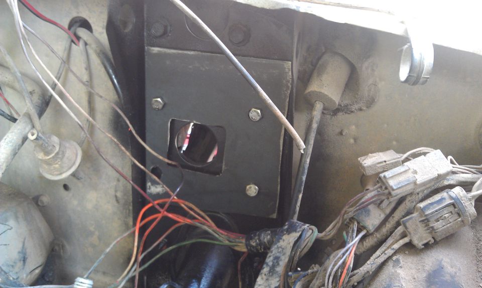 Close-up of vehicle firewall showing wiring harness and a metal plate with a circular opening