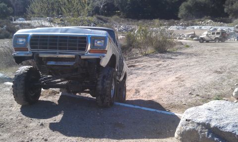 1978 Ford Bronco - A silver 1978 Ford Bronco navigates a rocky, off-road terrain with another vehicle visible in the background.