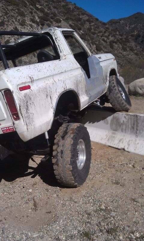 1978 Ford Bronco - White 1978 Ford Bronco navigating an off-road obstacle with its right front tire on a concrete barrier.