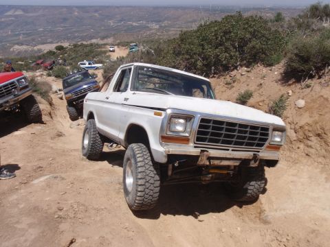1978 Ford Bronco - A group of off-road vehicles, including a white 1978 Ford Bronco, navigate a steep dirt trail.