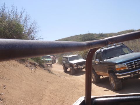 1978 Ford Bronco - A convoy of SUVs, including a dark green 1992 Ford Bronco, navigates a dusty off-road trail.