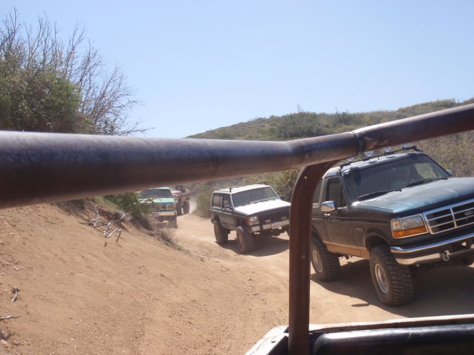 Dark green 1992 Ford Bronco driving on a dirt road with other SUVs