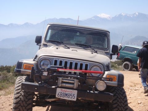 1978 Ford Bronco - Two off-road vehicles parked on a mountain trail with snowy peaks in the distance.