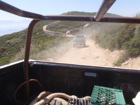 1978 Ford Bronco - Two trucks navigate a dusty, winding dirt road on a mountainside under a clear sky.