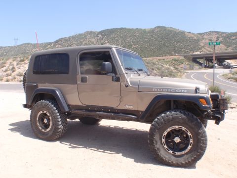 1978 Ford Bronco - This Jeep Wrangler Rubicon is parked off a dirt road with a highway overpass visible in the distance.