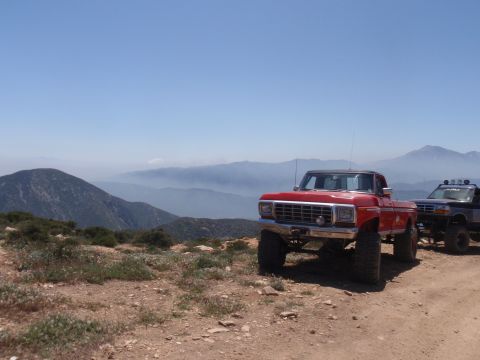 1978 Ford Bronco - Two off-road vehicles are parked on a mountain trail with a scenic view of distant mountains.