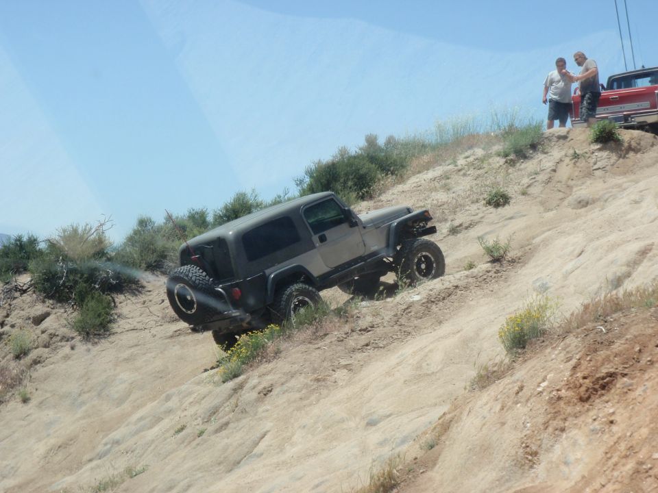 Gray Jeep Wrangler TJ climbing a dirt hill, two guys watching, red truck behind them