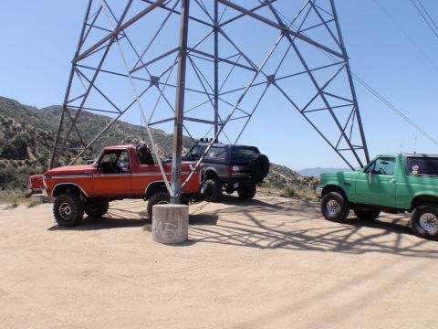1978 Ford Bronco - Three Ford Broncos are parked in a dusty, outdoor area beneath a large power line tower on a sunny day.