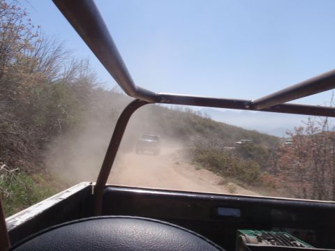 1978 Ford Bronco - Multiple vehicles travel on a dusty trail in a hilly, arid landscape.