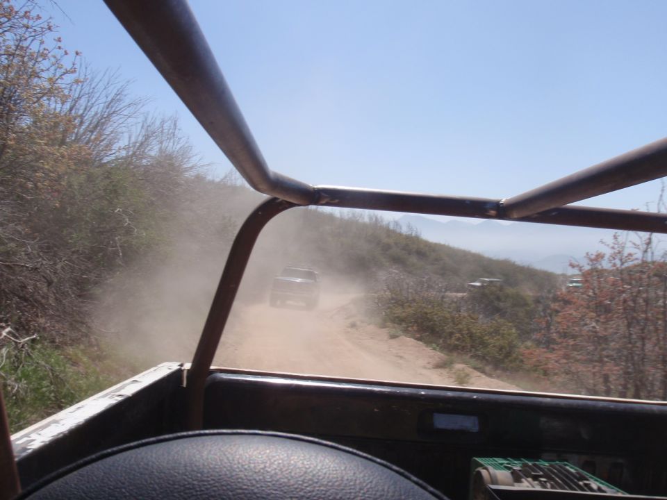 View from inside a vehicle looking out at a dusty off-road trail with other vehicles ahead