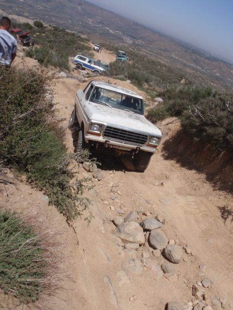 1978 Ford Bronco - A white 1978 Ford Bronco navigates a steep, rocky off-road trail with other vehicles in the background.