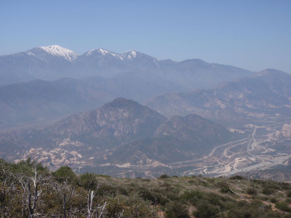 Mountain range with snow-capped peaks under a hazy blue sky, a highway winds through the valley below