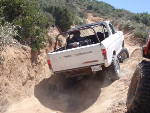 1978 Ford Bronco - A white SUV navigates a steep, dusty trail with another vehicle visible to the right.