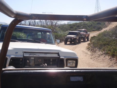1978 Ford Bronco - A 1978 Ford Bronco leads a convoy of off-road vehicles on a dusty dirt road under a clear sky.