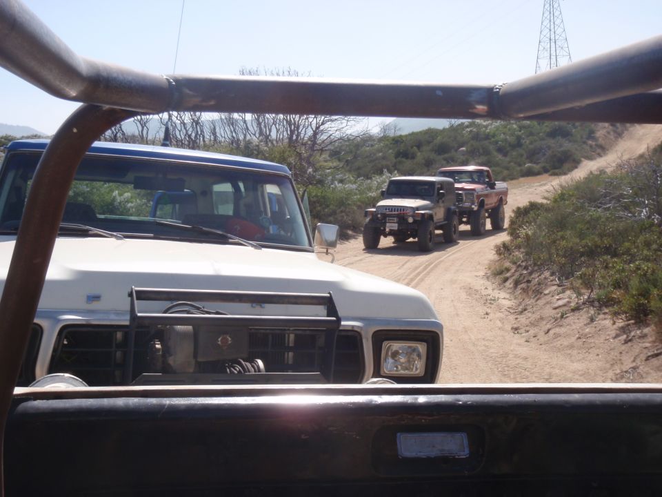 Front view of a 1978 Ford Bronco leading a convoy of off-road vehicles on a dirt road