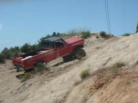 1978 Ford Bronco - A red pickup truck navigates a steep, rocky incline under a clear blue sky.