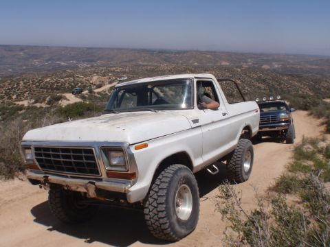 1978 Ford Bronco - A white 1978 Ford Bronco navigates a dusty off-road trail with a dark-colored SUV following closely behind.