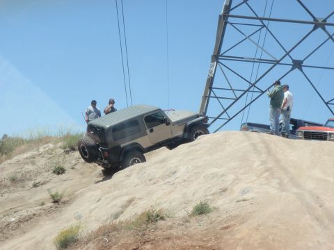 1978 Ford Bronco - A tan Jeep Wrangler navigates a steep dirt incline, with several people observing and other vehicles nearby.