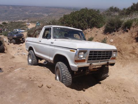 1978 Ford Bronco - A white 1978 Ford Bronco navigates a challenging off-road trail with other vehicles in the background.