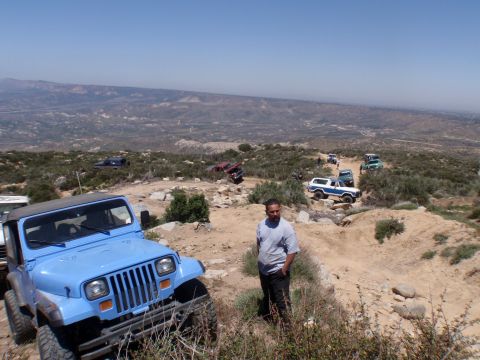 1978 Ford Bronco - Several off-road vehicles navigate a rocky trail on a hillside under a clear blue sky.