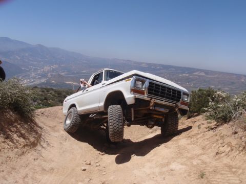 1978 Ford Bronco - White 1978 Ford Bronco navigating a challenging off-road trail under a clear blue sky.