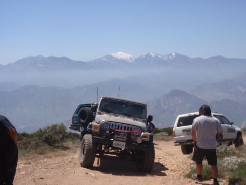 1978 Ford Bronco - Multiple off-road vehicles are parked on a dirt path with a mountainous landscape behind them.