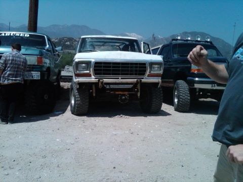 1978 Ford Bronco - Three lifted trucks, including a white 1978 Ford Bronco, are parked in an outdoor lot.