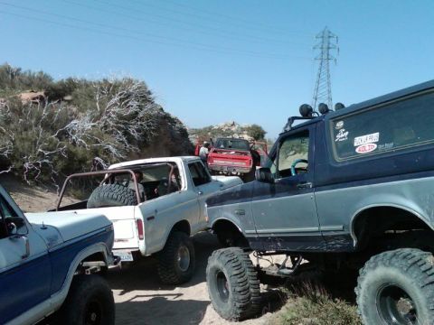 1978 Ford Bronco - Multiple off-road vehicles are gathered on a dusty trail under a clear blue sky.