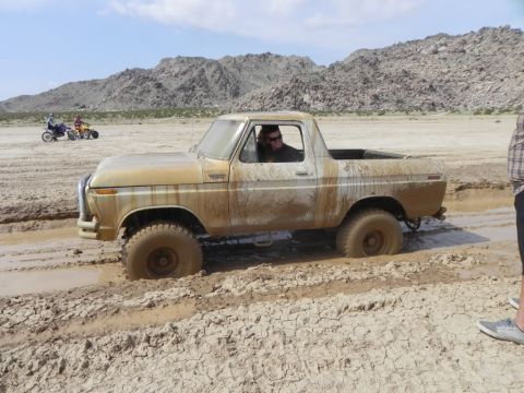 1978 Ford Bronco - A 1978 Ford Bronco is stuck in thick mud in a desert landscape, with two ATVs visible in the distance.