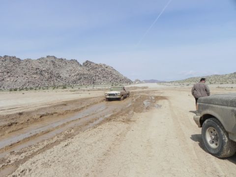 1978 Ford Bronco - A 1978 Ford Bronco navigates a muddy track in a desert landscape, with another vehicle nearby.