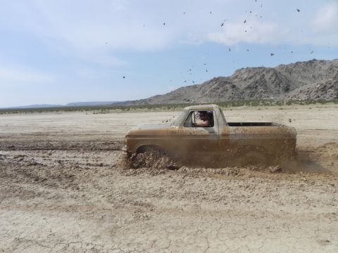 1978 Ford Bronco - A driver navigates a mud pit in a classic pickup truck under a bright, partly cloudy sky.