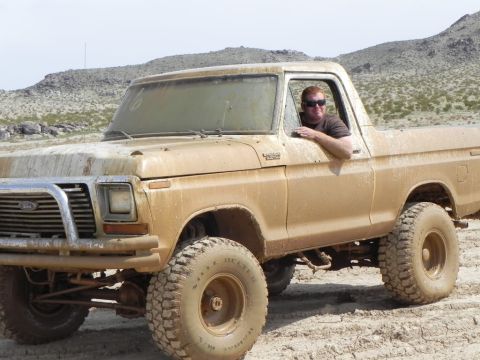 1978 Ford Bronco - A mud-covered 1978 Ford Bronco is driven by a man in a desert landscape.
