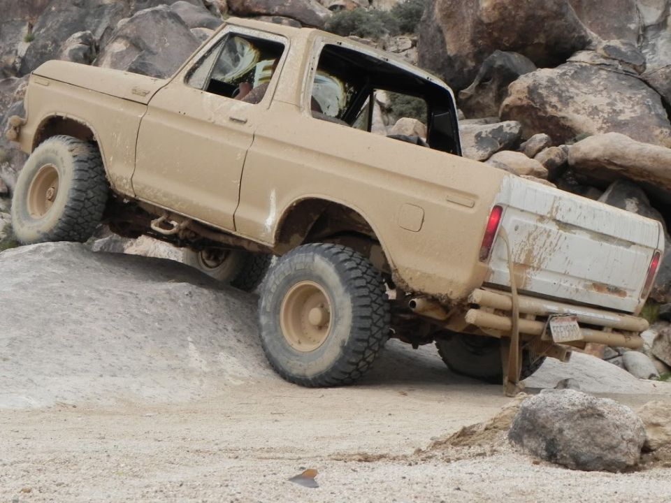 Tan 1978 Ford Bronco climbing a rocky incline, showing its off-road tires and suspension