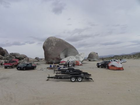 1978 Ford Bronco - A collection of vehicles and camping gear are set up in a desert area, with prominent rock formations in the background.