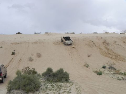 1978 Ford Bronco - Two trucks navigate a sandy incline in a desert landscape under an overcast sky.