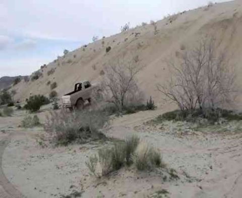 1978 Ford Bronco - A white pickup truck navigates a sandy incline in a desert landscape, with a "SUPERMOTORS" logo visible in the lower right corner.